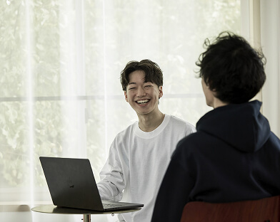 ノートパソコンを前に笑顔の男性と後ろ姿の男性の写真